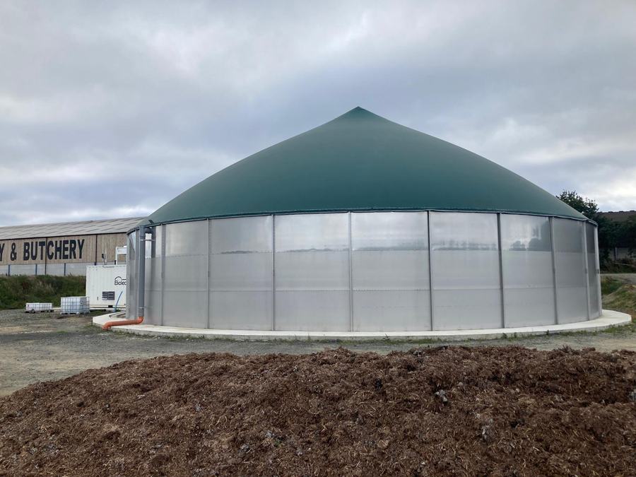 A completed digester with dome roof beside farm buildings