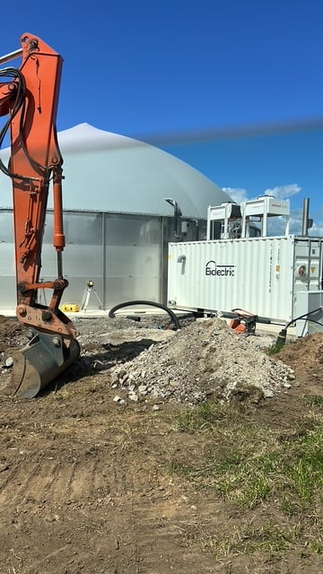 An excavator on site alongside a partly built digester and Biolectric container