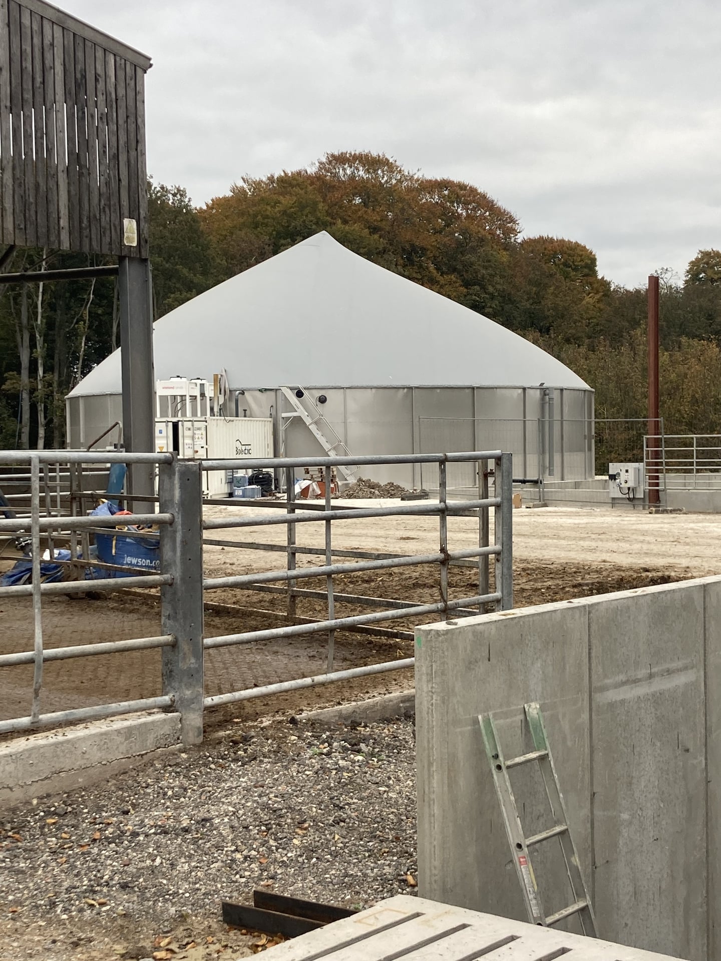 A near-complete digester tank with white cover, alongside farm livestock pens